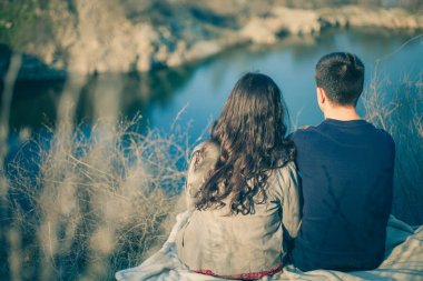 Karı koca göl kıyısında kayalık sahiller, erken Bahar ile. Suya bir göl günbatımı arka plan üzerinde gitmek aşıkların siluetleri.