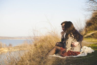 Karı koca göl kıyısında kayalık sahiller, erken Bahar ile. Suya bir göl günbatımı arka plan üzerinde gitmek aşıkların siluetleri.