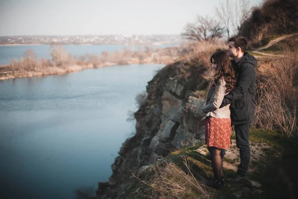 Esposo y esposa en la orilla del lago con costas rocosas, principios de primavera. Siluetas de amantes que entran en el agua sobre el fondo de la puesta de sol sobre un lago . — Foto de Stock