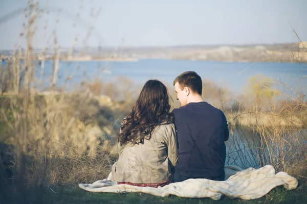 Man en vrouw aan de oever van het meer met rotsachtige kusten, in het vroege voorjaar. Silhouetten van liefhebbers die gaan in het water op de achtergrond van de zonsondergang op een meer. — Stockfoto