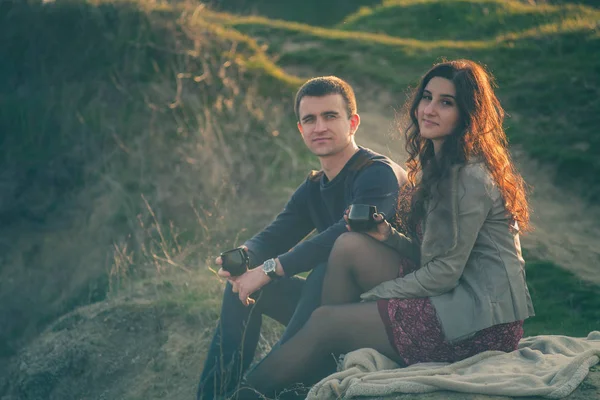 loving young couple happy together outdoor, drinking tea. A guy with a girl on the lake at sunset drinks tea.