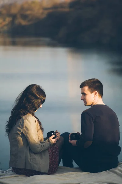 Amante joven pareja feliz juntos al aire libre, beber té. Un tipo con una chica en el lago al atardecer bebe té. . — Foto de Stock
