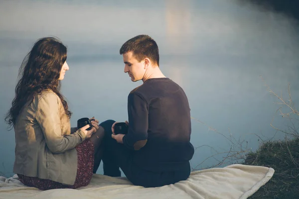 Amante joven pareja feliz juntos al aire libre, beber té. Un tipo con una chica en el lago al atardecer bebe té. . — Foto de Stock