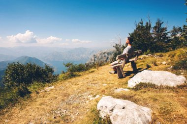 Adam içinde belgili tanımlık geçmiş Bay Karadağ'daki dağlarda. Kotor Koyu'ndaki dağlarında bir bankta bir adam oturuyor