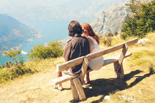 Un tipo con una chica está sentado en un banco en Kotor Bay. Familia feliz de cuatro caminando por las montañas. Concepto familiar. Viaje en familia . — Foto de Stock