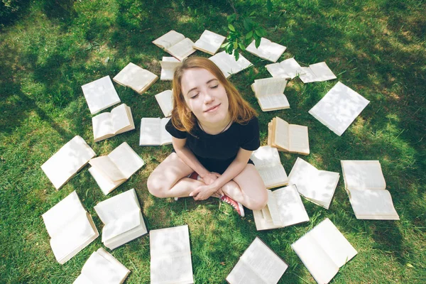 Young girl reading a book while lying in the grass. A girl among the books in the summer garden — Stock Photo, Image