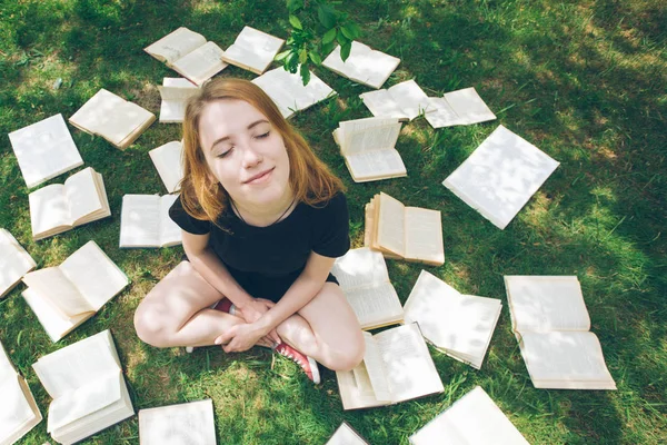 Молодая девушка читает книгу, лежа на траве. Девушка среди книг в летнем саду — стоковое фото