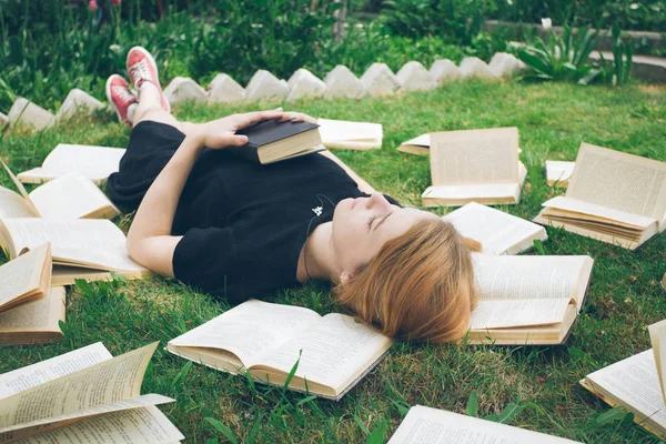 Jong meisje het lezen van een boek tijdens het liggen in het gras. Een meisje tussen de boeken in de zomertuin — Stockfoto