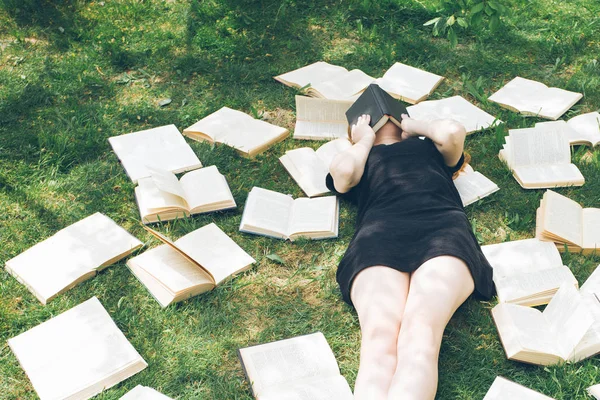 Rapariga a ler um livro enquanto deitada na relva. Uma menina entre os livros no jardim de verão — Fotografia de Stock