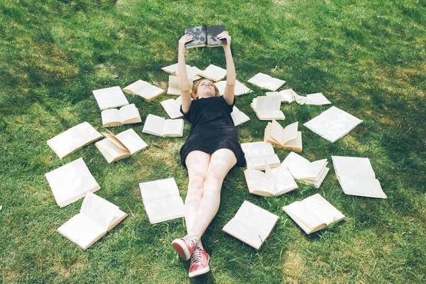 Rapariga a ler um livro enquanto deitada na relva. Uma menina entre os livros no jardim de verão — Fotografia de Stock