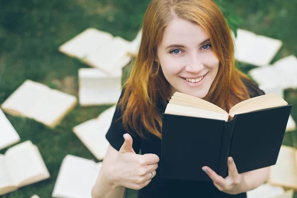 Rapariga a ler um livro enquanto deitada na relva. Uma menina entre os livros no jardim de verão — Fotografia de Stock