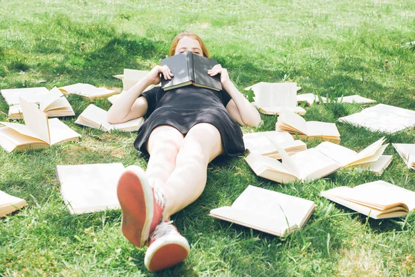 Jong meisje het lezen van een boek tijdens het liggen in het gras. Een meisje tussen de boeken in de zomertuin — Stockfoto