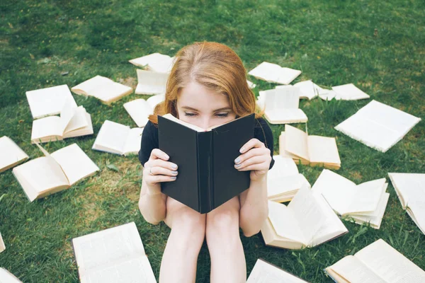 Jong meisje het lezen van een boek tijdens het liggen in het gras. Een meisje tussen de boeken in de zomertuin Stockafbeelding