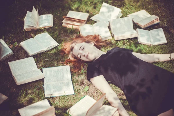 Rapariga a ler um livro enquanto deitada na relva. Uma menina entre os livros no jardim de verão — Fotografia de Stock