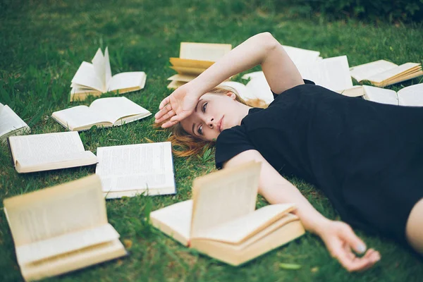Rapariga a ler um livro enquanto deitada na relva. Uma menina entre os livros no jardim de verão — Fotografia de Stock