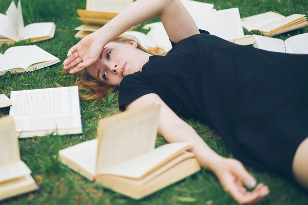 Rapariga a ler um livro enquanto deitada na relva. Uma menina entre os livros no jardim de verão — Fotografia de Stock