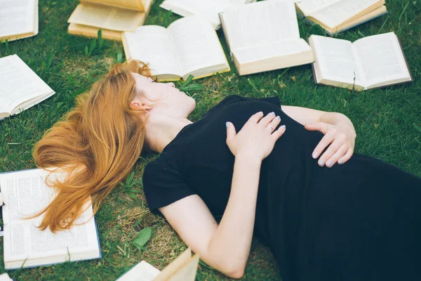 Rapariga a ler um livro enquanto deitada na relva. Uma menina entre os livros no jardim de verão — Fotografia de Stock