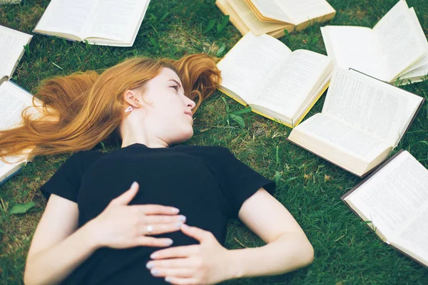 Rapariga a ler um livro enquanto deitada na relva. Uma menina entre os livros no jardim de verão — Fotografia de Stock