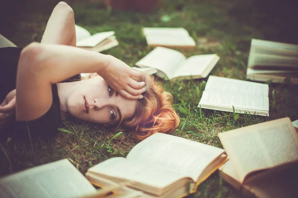 Rapariga a ler um livro enquanto deitada na relva. Uma menina entre os livros no jardim de verão — Fotografia de Stock