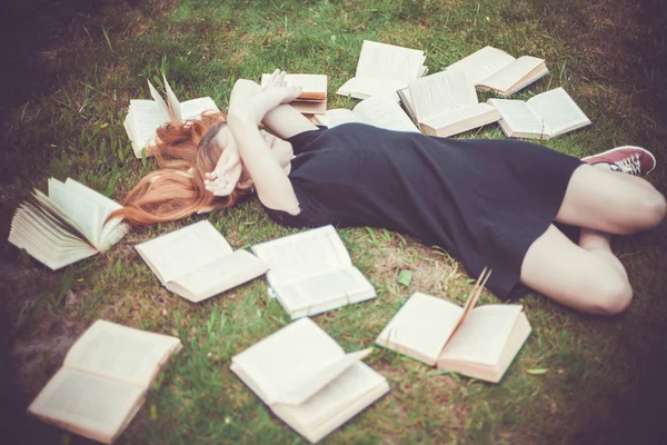 Rapariga a ler um livro enquanto deitada na relva. Uma menina entre os livros no jardim de verão — Fotografia de Stock