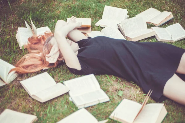 Rapariga a ler um livro enquanto deitada na relva. Uma menina entre os livros no jardim de verão — Fotografia de Stock