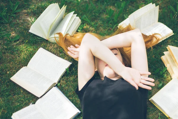 Rapariga a ler um livro enquanto deitada na relva. Uma menina entre os livros no jardim de verão — Fotografia de Stock