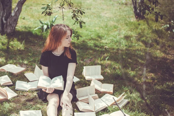 Nuori tyttö lukee kirjaa, kun makaa nurmikolla. Tyttö joukossa kirjoja kesäpuutarhassa — kuvapankkivalokuva