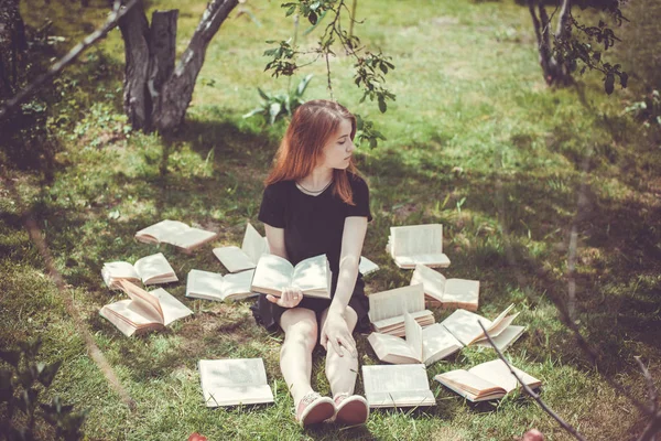 Rapariga a ler um livro enquanto deitada na relva. Uma menina entre os livros no jardim de verão — Fotografia de Stock