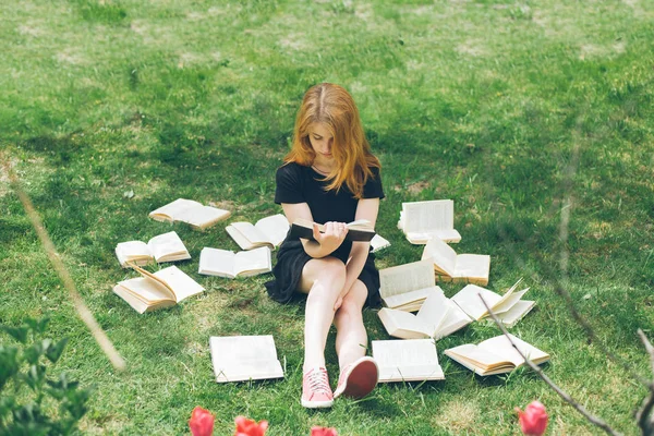 Rapariga a ler um livro enquanto deitada na relva. Uma menina entre os livros no jardim de verão — Fotografia de Stock