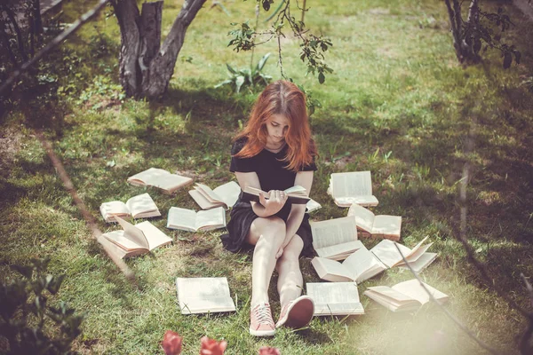 Rapariga a ler um livro enquanto deitada na relva. Uma menina entre os livros no jardim de verão — Fotografia de Stock