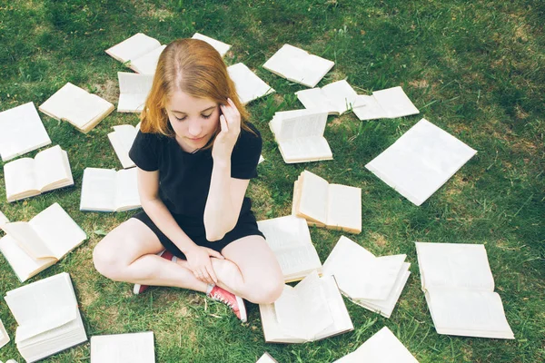 Młoda dziewczyna czytając książkę leżąc na trawie. Dziewczyna wśród książek w ogrodzie — Zdjęcie stockowe