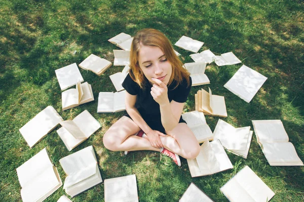 Rapariga a ler um livro enquanto deitada na relva. Uma menina entre os livros no jardim de verão — Fotografia de Stock