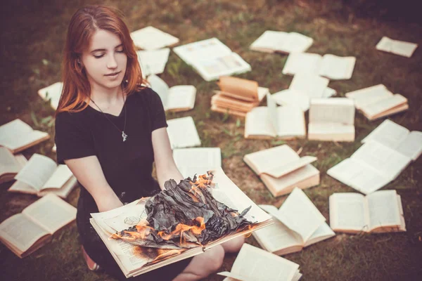 Uma menina segurando um livro queimando na natureza no jardim de verão — Fotografia de Stock