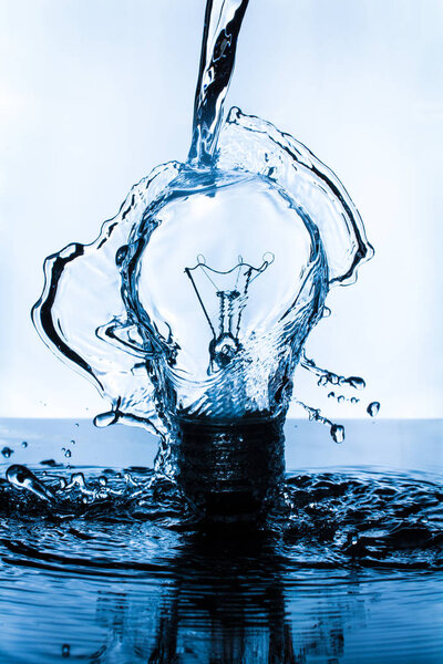 Lightbulb splashed with water on dark surface with blue hue