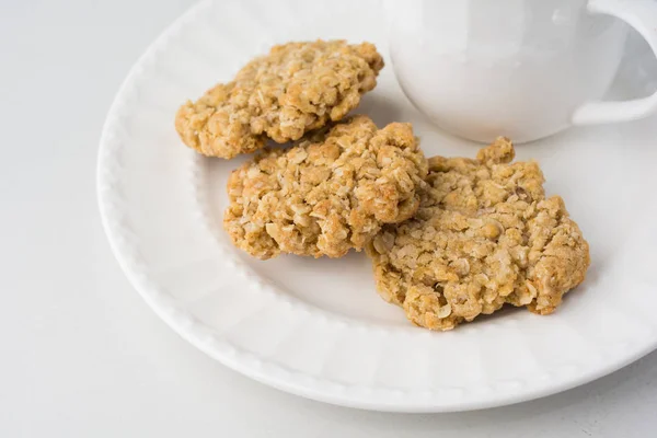 Three oatmeal cookies on white plate with teacup — Stock Photo, Image