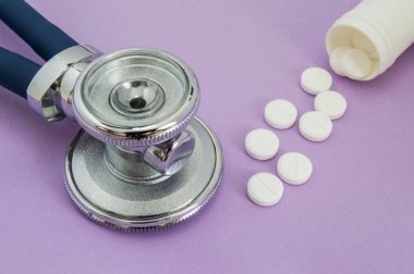 Bir plastik tüp veya kavanoz ve steteskop başkanı dışarı mor bir arka plan üzerine düşen beyaz hap. Çerçeve veya iç hastalıkları ve kardiyovasküler yönü için resme