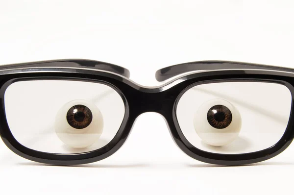 Figuras olhos ou globos oculares estão por trás de óculos de aros pretos em um vidro ligeiramente escurecido em um fundo branco. Foto conceitual para oftalmologia, optometria, seleção de óculos para corrigir ou boa visão — Fotografia de Stock