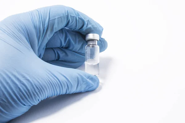 Flacon transparent ou une bouteille avec le vaccin est dans la main du médecin, qui est habillé de gants médicaux bleus. Le concept de vaccination, de recherche ou de production de vaccins contre diverses maladies — Photo