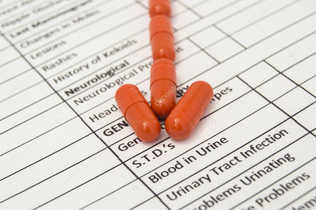 Arrow of orange antibiotic capsules indicates word STDs specified on a sheet of health history. Medications for the treatment of sexually transmitted diseases and other urological diseases