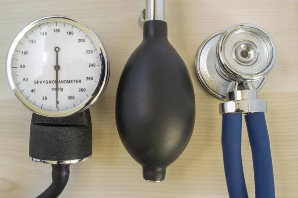 Stethoskop oder Phonendoskop, mechanisches Manometer zur Messung des Blutdrucks und Glühbirne mit Luftventil liegen auf einem Holztisch in der Arztpraxis. Blutdruck messen — Stockfoto