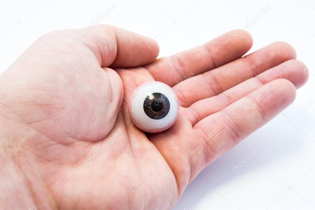Anatomical model of eyeball or eye prosthesis lies on open palm of doctor hands. Photos for use in eye surgery, ophthalmology, trauma and care of eyes, vision, eye-hand  coordination or Hamsa amulet