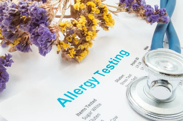 Printed result of allergy test (blood or skin) lies next to flowers with falling pollen and stethoscope. Concept photo for analysis of presence allergies to food, pollen, hair or wools in human