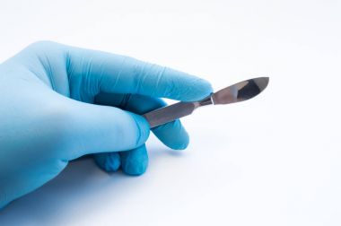 Hand holding scalpel. Palm of surgeon dressed in blue glove holding scalpel. Concept photo for surgeries, procedures, treatment, plastic surgery operation, work of surgical departments and hospitals clipart