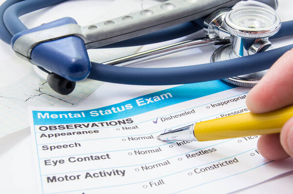 Scene from workplace neurologist or psychiatrist. Neurologist checkout process patient data of mental status test or exam which lies on workplace with stethoscope, neurological hammer and ECG ribbon