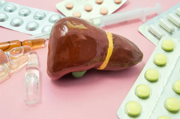 Liver treatment concept photo. Figure liver surrounded by pills, medications, medicine vials with syringe, symbolizing treatment, prevention and protection of liver from bacteria, viruses and toxins — Stock Photo, Image