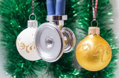 Tıbbi Noel ve yeni yıl. Beyaz ve altın Noel ağacı topları ile çevrili stetoskop Noel dekorasyonu arka plan - yeşil çelenk üzerinde bulanık. Tıpta yeni yıl için kavram