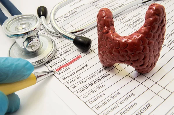 Thyroïde problèmes concept photo. Le médecin pointe dans le processus de diagnostic à l'inscription des problèmes thyroïdiens sur la feuille d'antécédents médicaux du patient, qui se trouve près de la forme de la glande thyroïde et stéthoscope — Photo