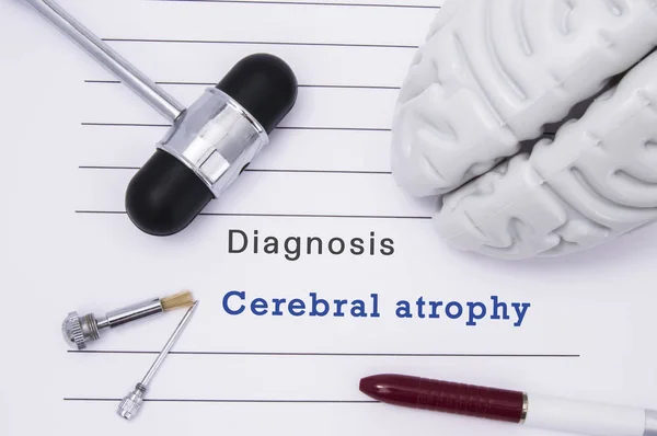 Diagnóstico de atrofia cerebral. O martelo neurológico e a figura do cérebro encontram-se em um formulário médico do papel com um diagnóstico da posição da atrofia cerebral em uma tabela no escritório de um neurologista — Fotografia de Stock