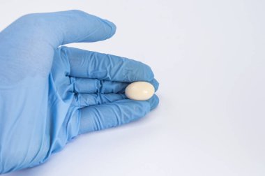 Soft gelatin vaginal tablet or suppository in the hand of the gynecologist, dressed in a blue latex glove. Treatment of diseases of the reproductive organs of women and prevention of women's health clipart