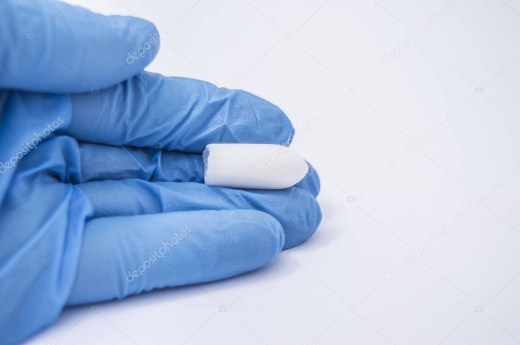 Soft suppository with medicine (laxative or to treat proctological diseases) lies in the hand of the doctor proctologist that dressed in blue medical glove